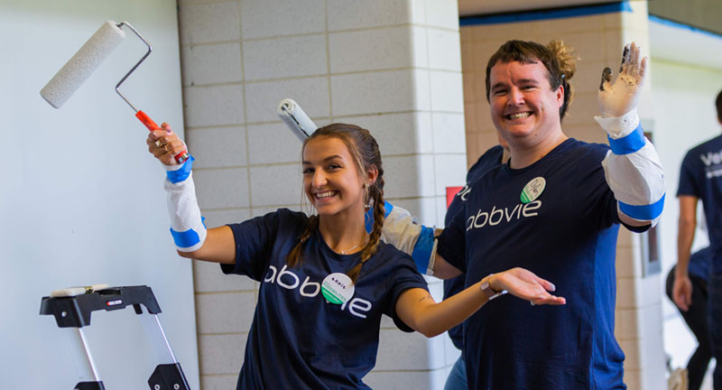 Man and woman in AbbVie shirts smiling while holding paint rollers