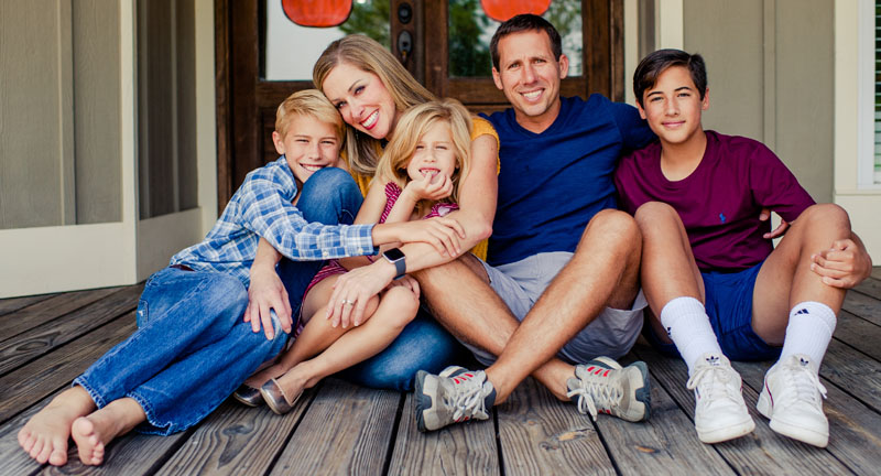 A mother and father smiling with their two sons and daughter on a wooden porch